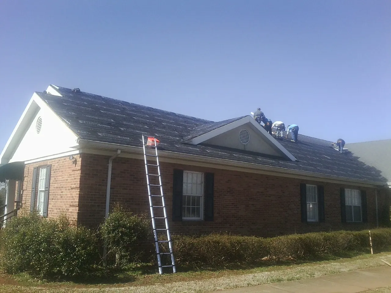 Crew tearing shingles off a brick ranch roof with a ladder set — Emergency Roof Repair work by our crew in Guthrie