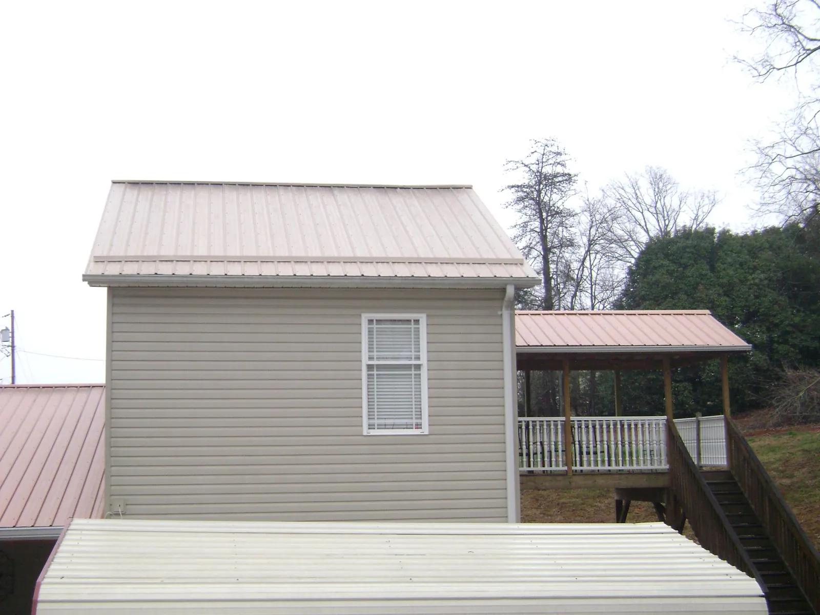 Tan metal roofs on a two story addition and attached porch, from a Roof Replacement job in Guthrie